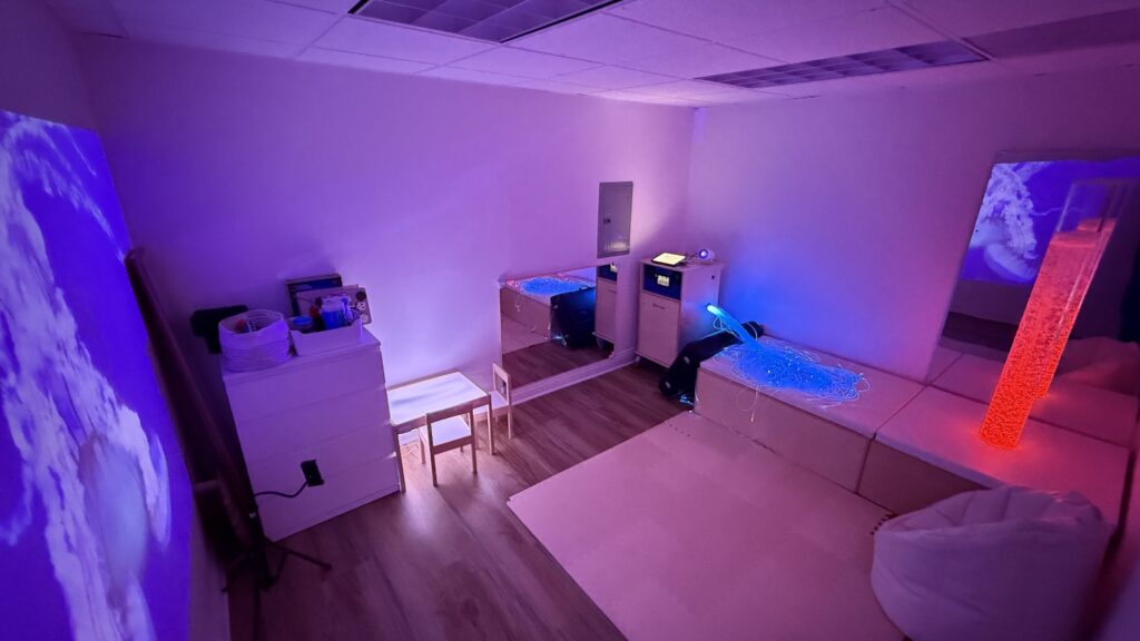 Sensory room with a bubble column, fiber optic lights, mirrors and wall projections at Sensory Bridge Pediatric Therapy.