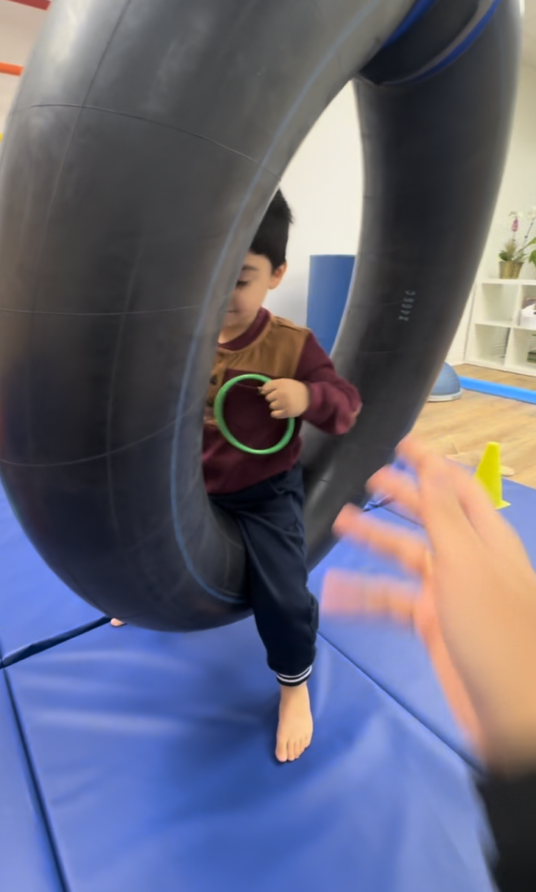Child seated inside a tire swing holding a green ring.