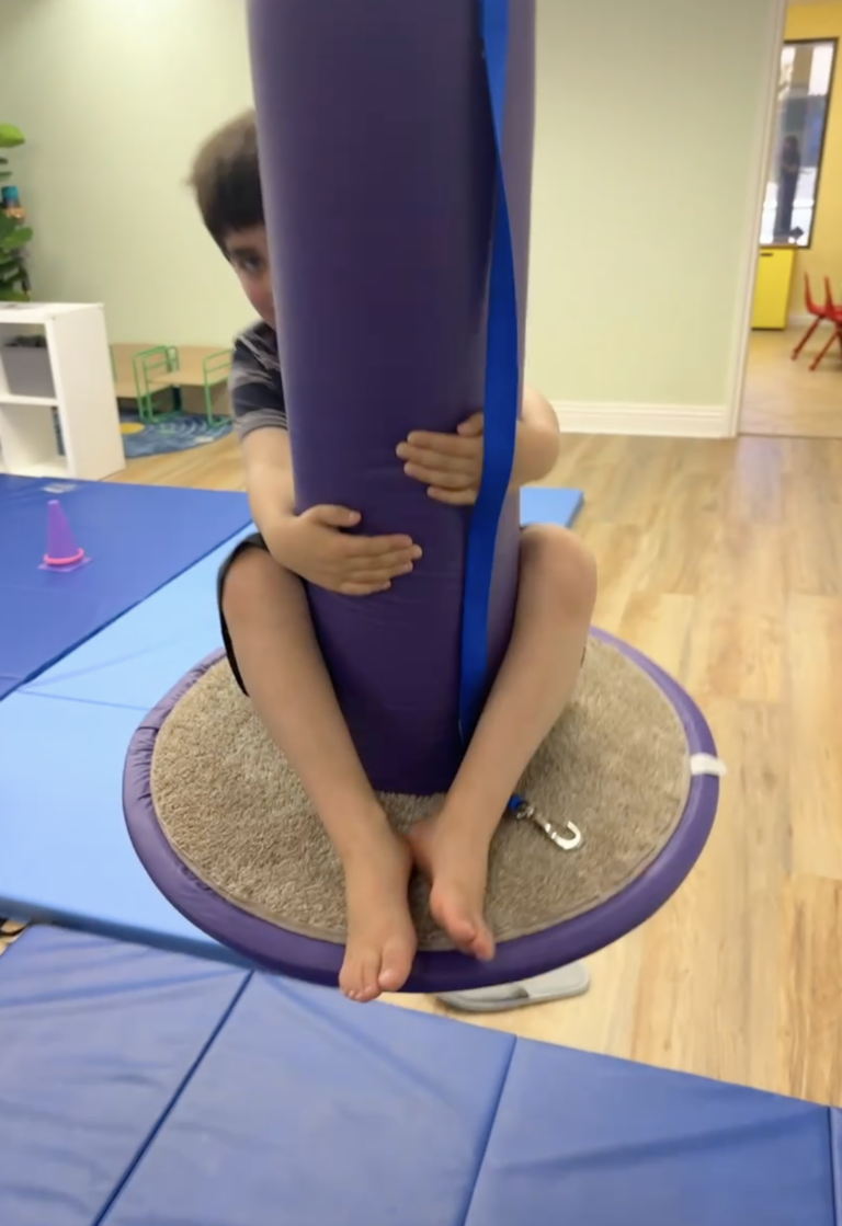 Child seated on a purple bolster swing.
