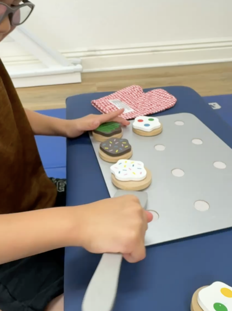 Hands using a spatula with a wooden pretend cookie set.