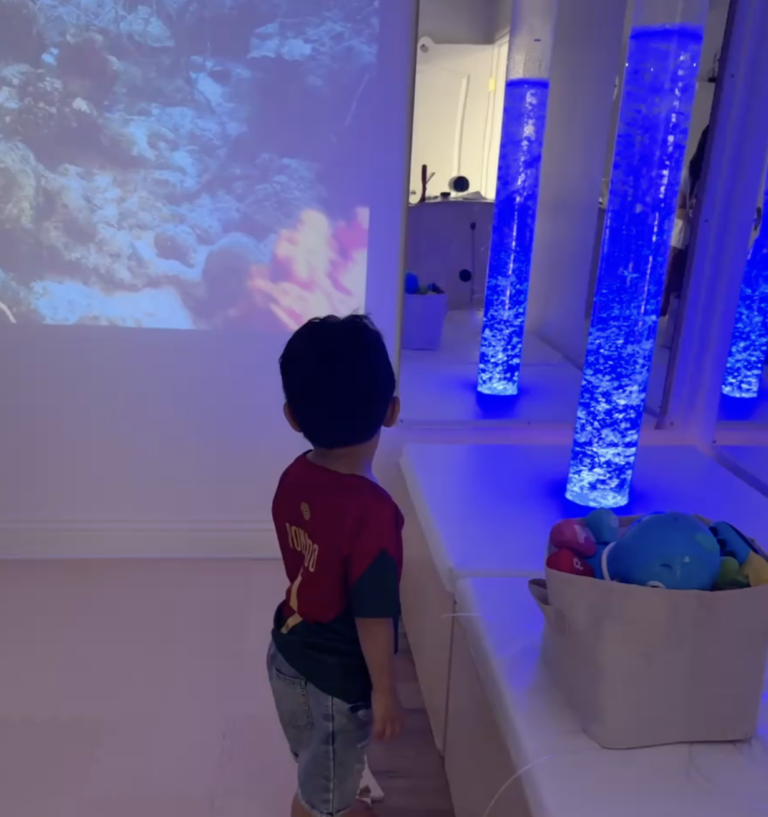 Child exploring a room with blue bubble columns and projected lights.