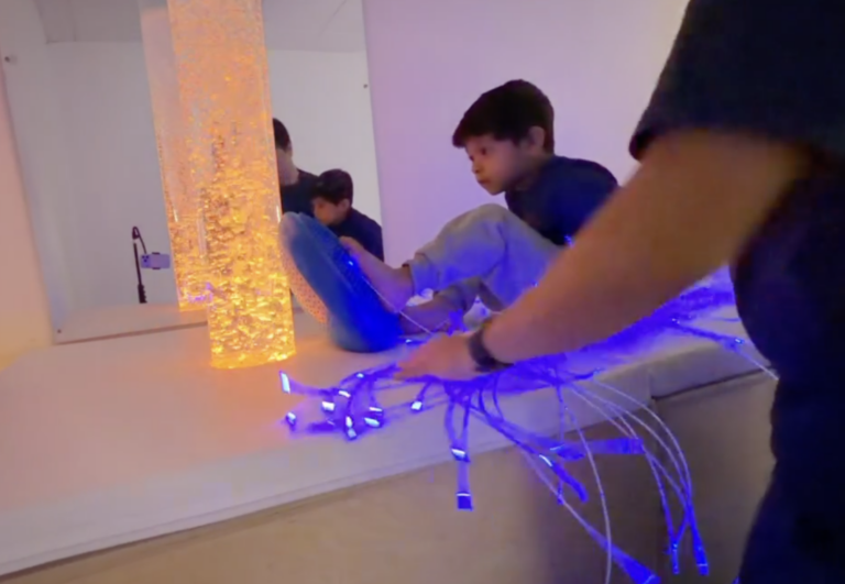 Therapist and child beside an amber bubble column and blue fiber optic strands.