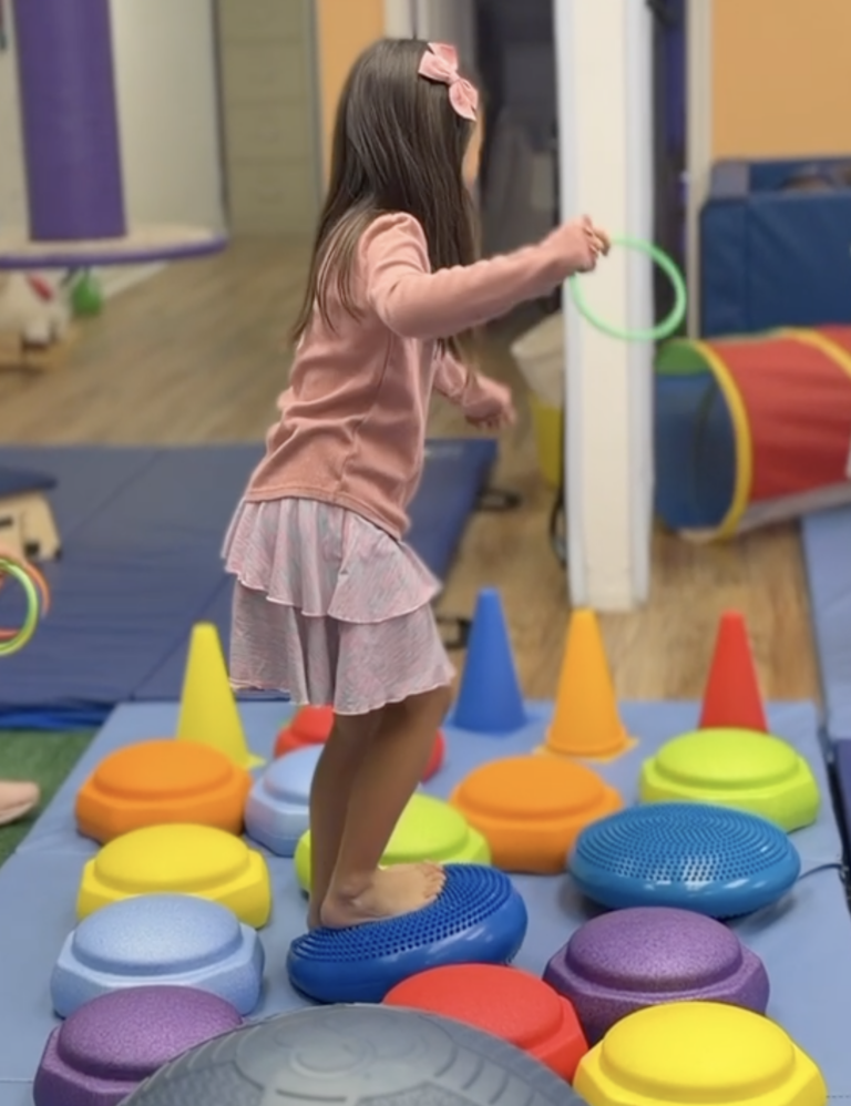 Child standing on blue balance pods while holding a green ring.