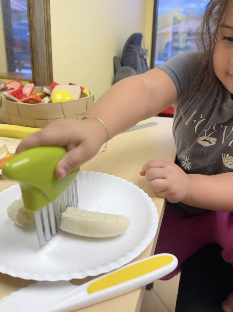 Child uses a food cutter to explore a banana during SOS feeding therapy.