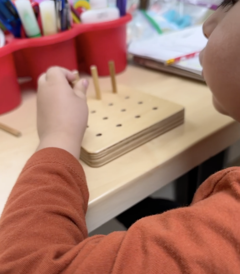Child working with a wooden pegboard at a desk.