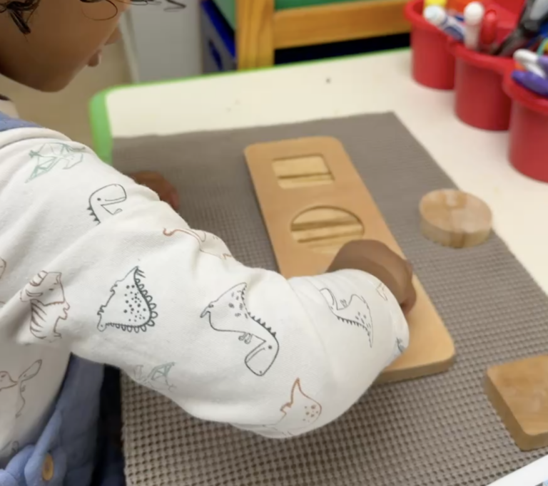 Child working with a wooden shape puzzle at a desk.