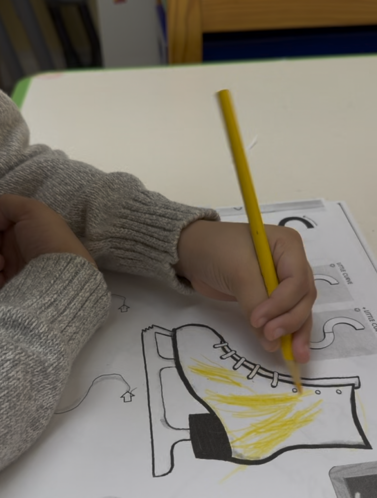 Hand using a yellow pencil to color an ice skate worksheet.