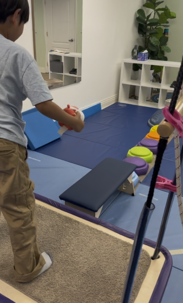 Child holding a red toy while seated on a platform swing.