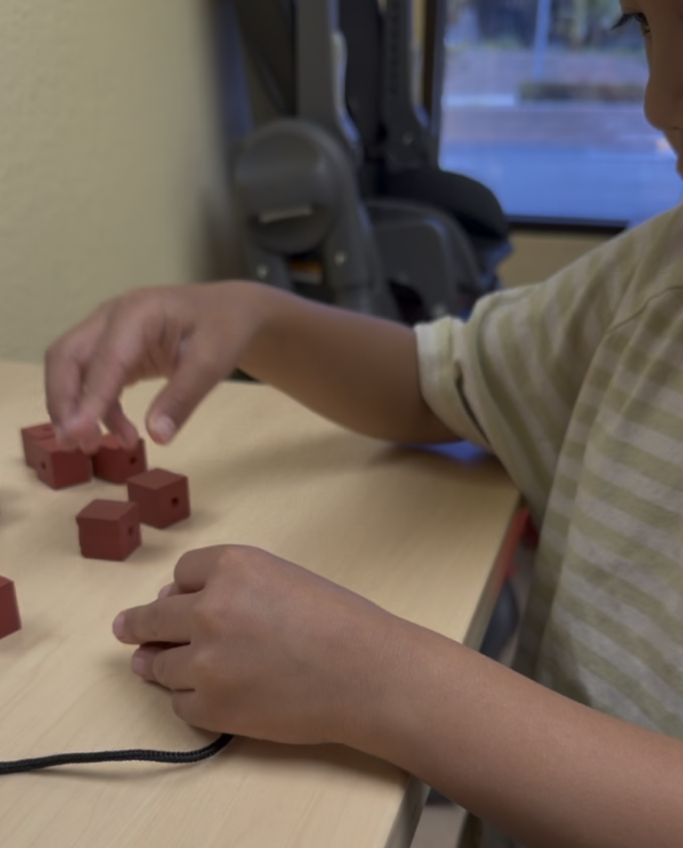 Child working with small red blocks and thread at a table.