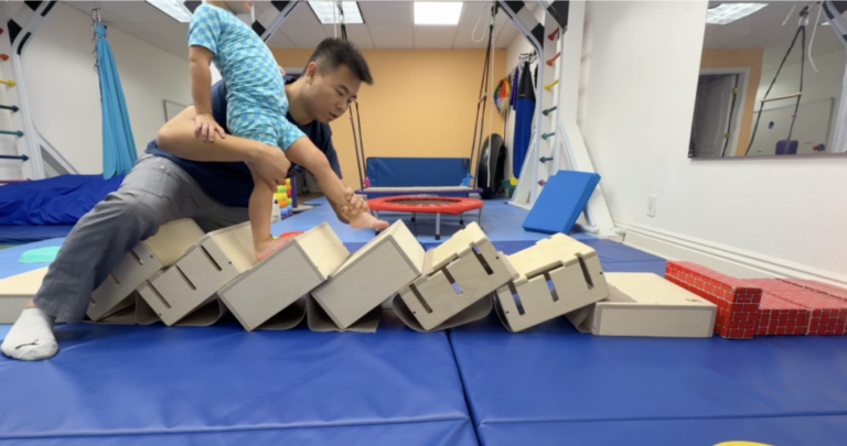DMI movement practice with a therapist supporting a child across angled wooden boxes.
