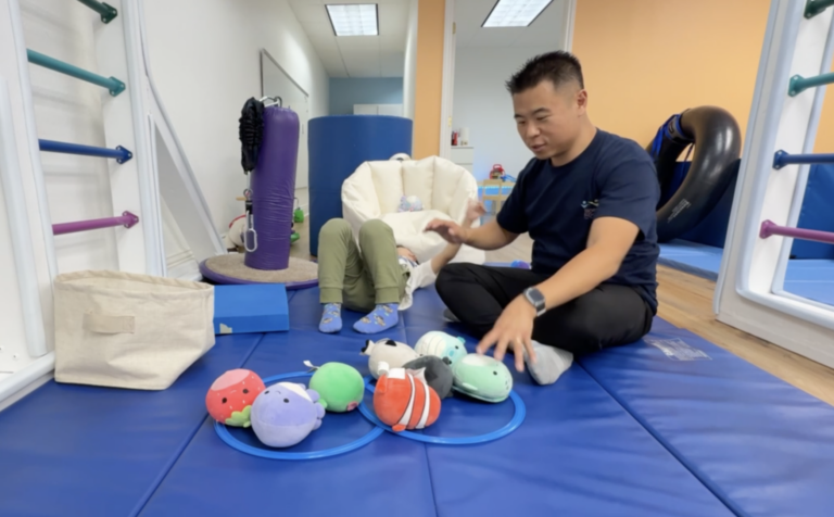 Therapist and child during floor play with plush animals and rings.