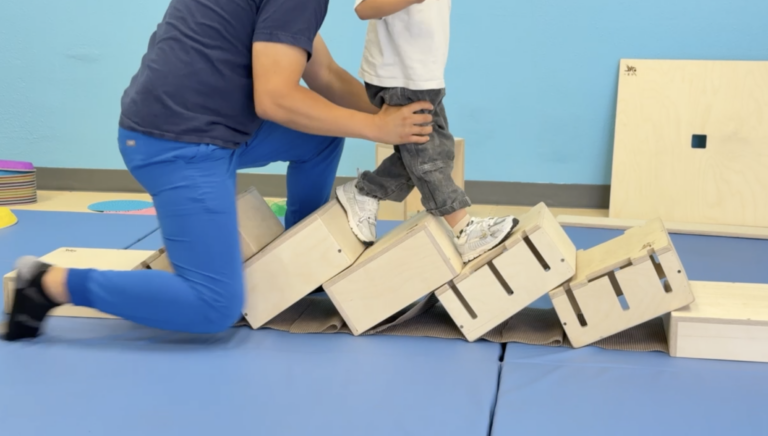 Close view of a therapist supporting a child stepping across angled DMI boxes.