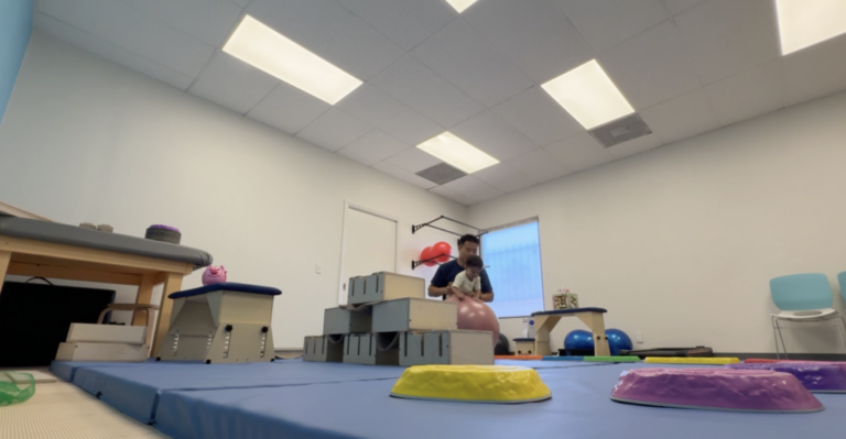 Wide view of the therapy gym with a therapist and child using a pink therapy ball.