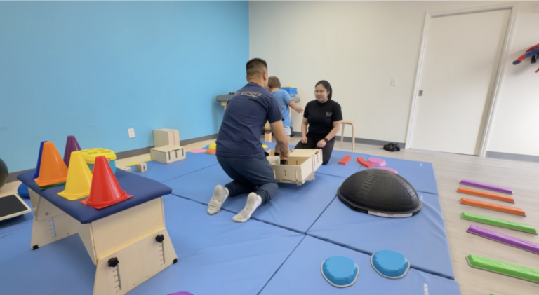Therapists supporting a child moving through wooden DMI box activities.