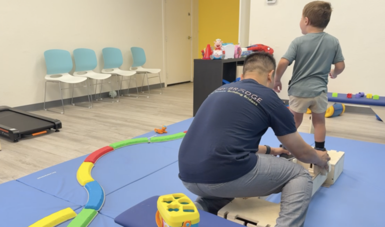Therapist supporting a child standing on a wooden DMI platform.