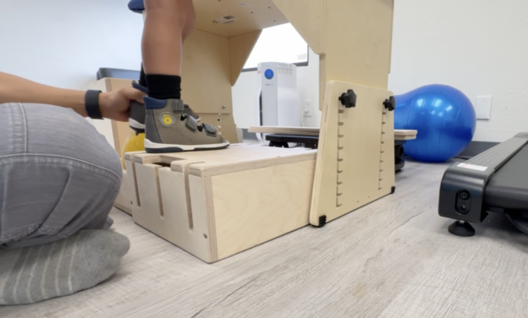 Close view of a therapist supporting a child's ankle on a wooden DMI platform.
