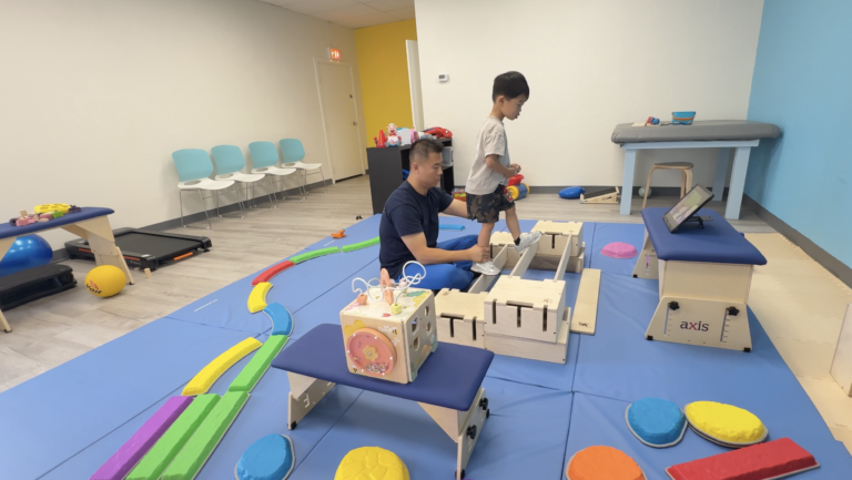 Therapist supporting a child standing on parallel wooden DMI beams.