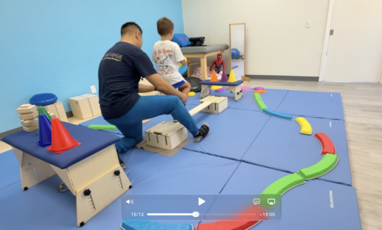 Therapist supporting a child practicing on a narrow wooden DMI beam.