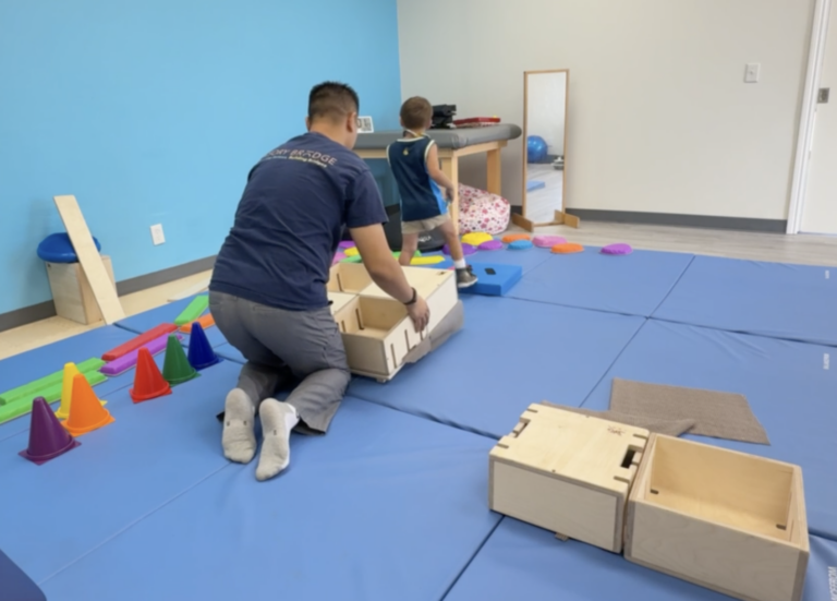 Therapist supporting a child moving through wooden DMI box activities.
