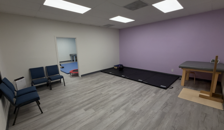 Therapy room with a purple wall, floor mats, chairs and a treatment table.