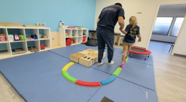 Therapist helping a child walk along a colorful stepping path.