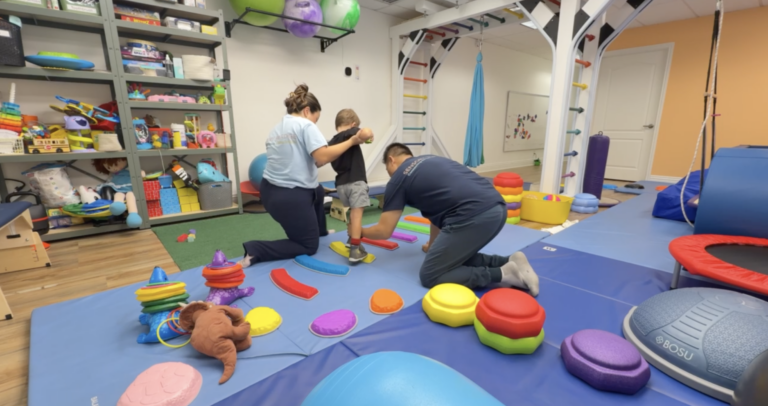 Two therapists supporting a child on a colorful stepping path in the sensory gym.